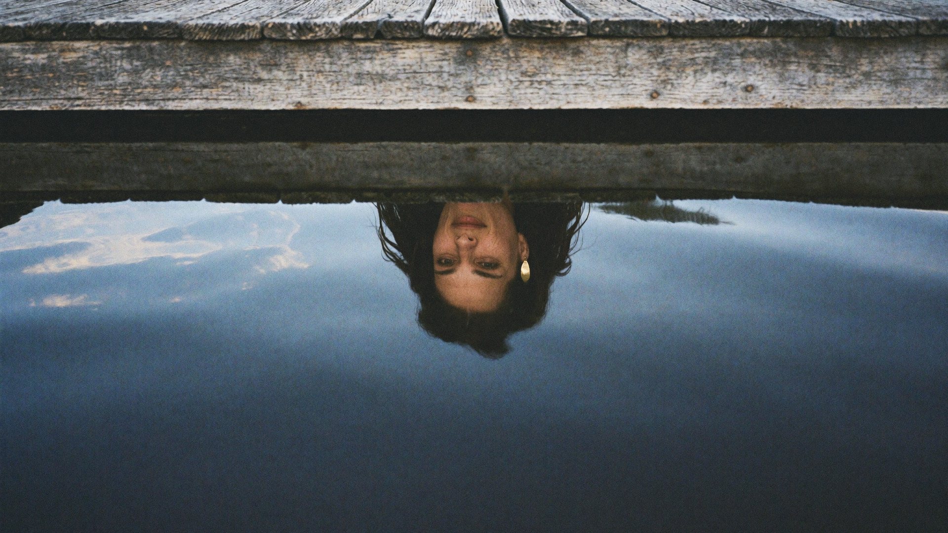 Lizzy Veyra's reflection in the still river beneath a wooden dock.