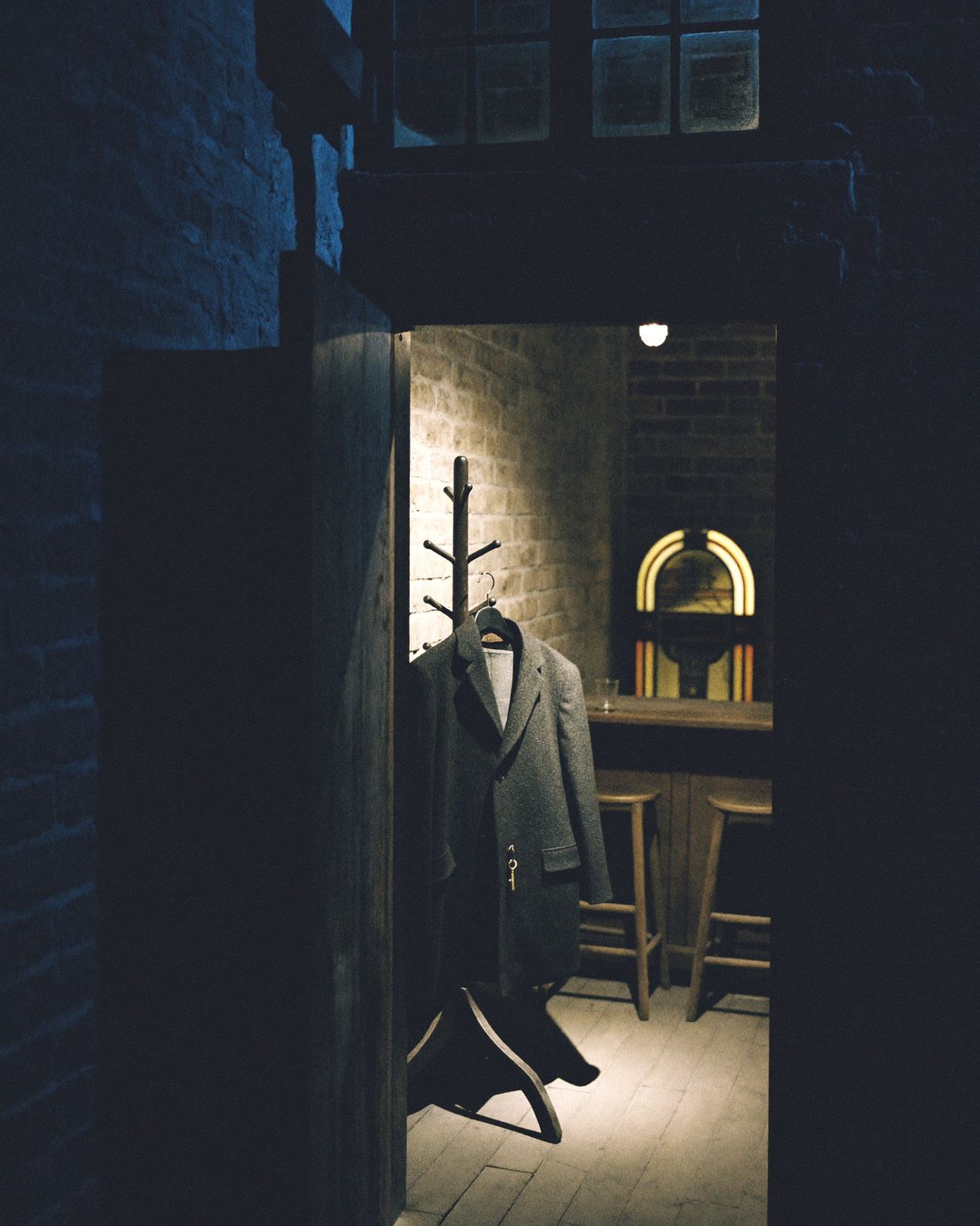 A dark coat hanging alone in an empty bar at night, seen through a half-open door.